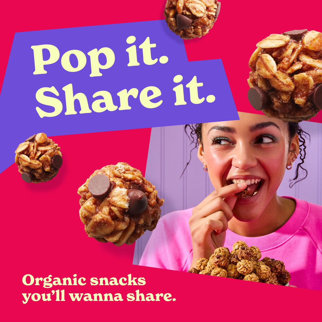 A bold and colorful promotional image featuring a smiling woman in a pink sweatshirt enjoying a bite-sized oat and chocolate snack. Surrounding her are floating snack bites, highlighting their texture and ingredients. A purple speech bubble with large, playful text reads, "Pop it. Share it." Below, white text on a red background emphasizes, "Organic snacks you’ll wanna share." The composition is fun and energetic, reinforcing the snack’s appeal.