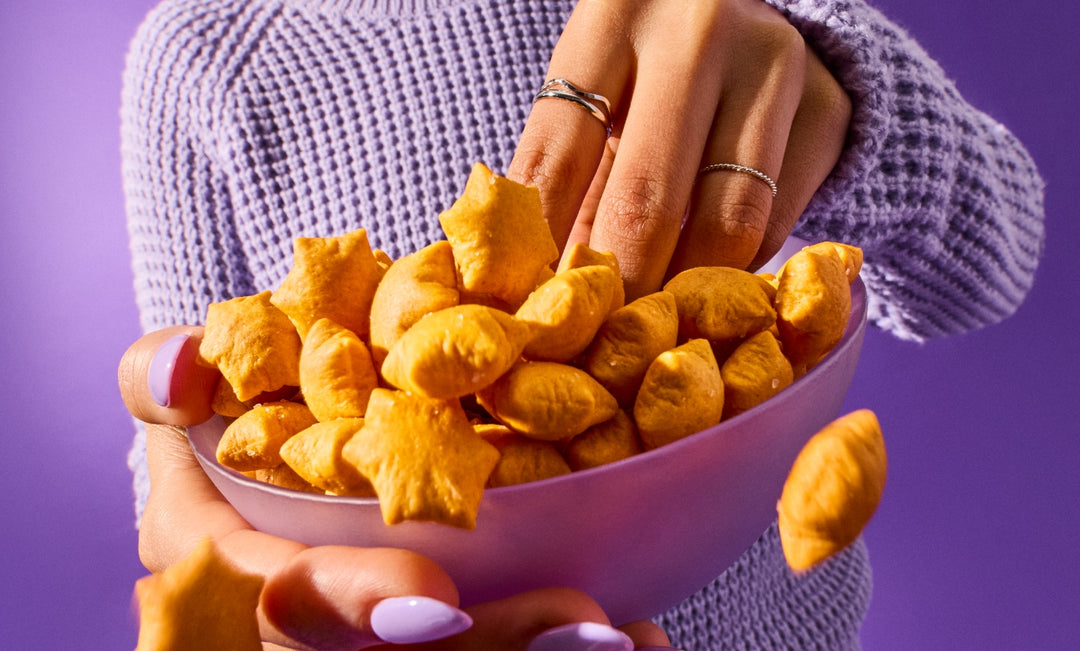 A person wearing a purple sweater reaches into an overflowing bowl of star puffed crackers.