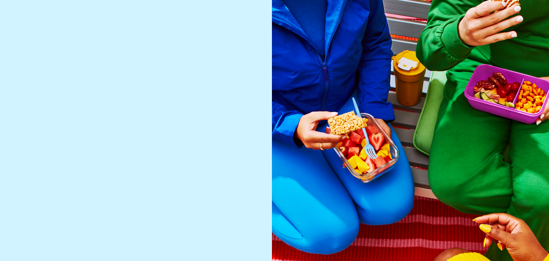 Two people sit side-by-side, one in blue with a fruit bowl and coffee cup, the other in green with a purple tray of strawberries and snacks. Casual and relaxed setting.