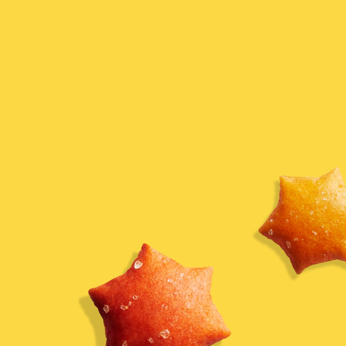 A close up of MadeGood star puffed crackers showing its texture and salt crystals, set on a yellow background