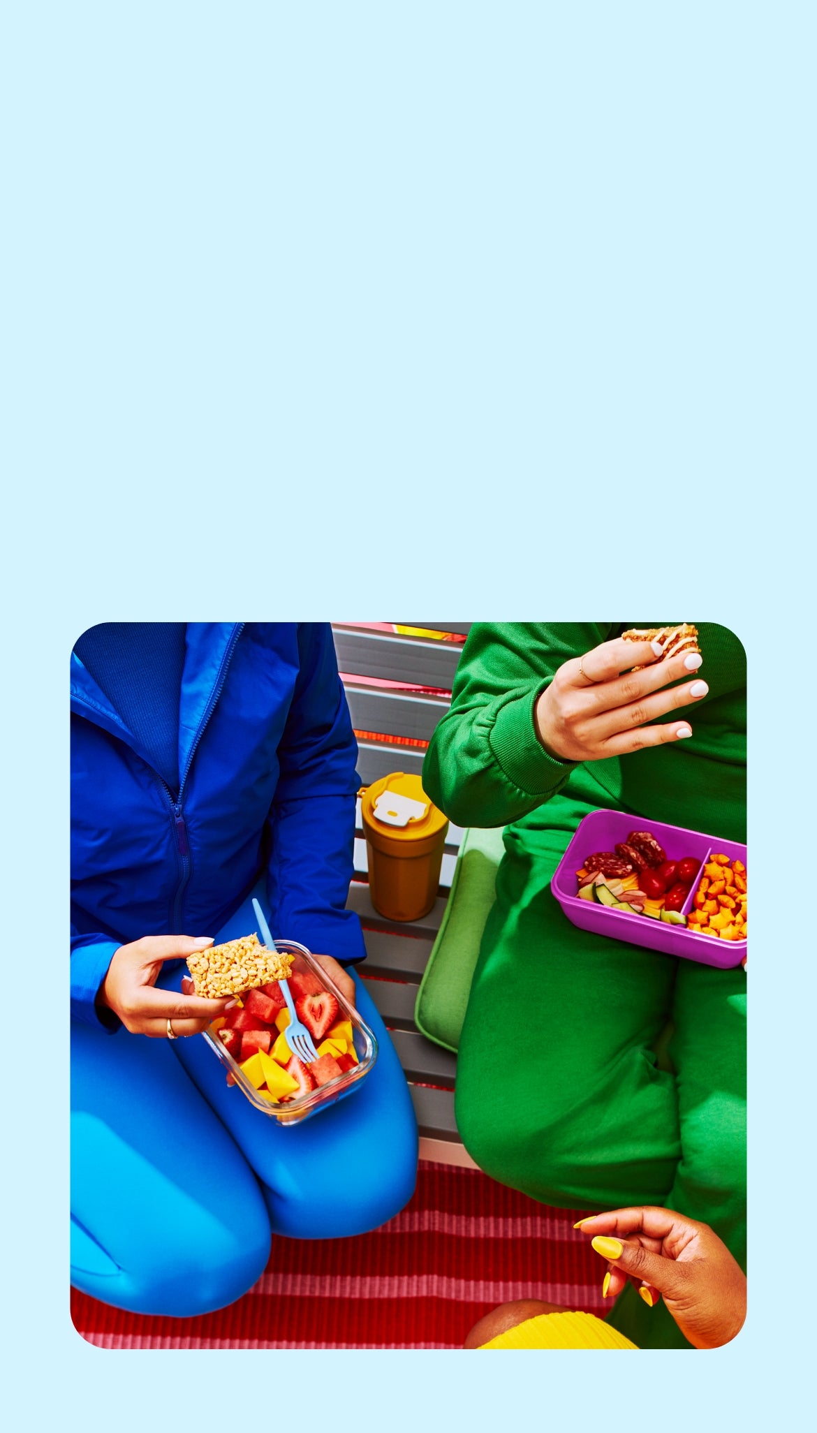 A picnic scene depicts 3 people seated on a striped blanket with fruits, vegetables and crackers visible