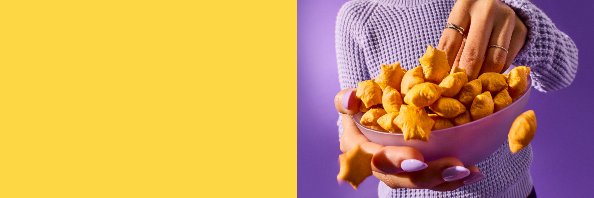 A person wearing a purple sweater reaches into an overflowing bowl of star puffed crackers.