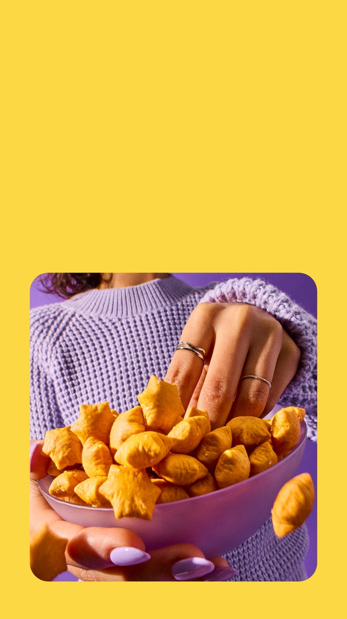 A person wearing a purple sweater reaches into an overflowing bowl of star puffed crackers.