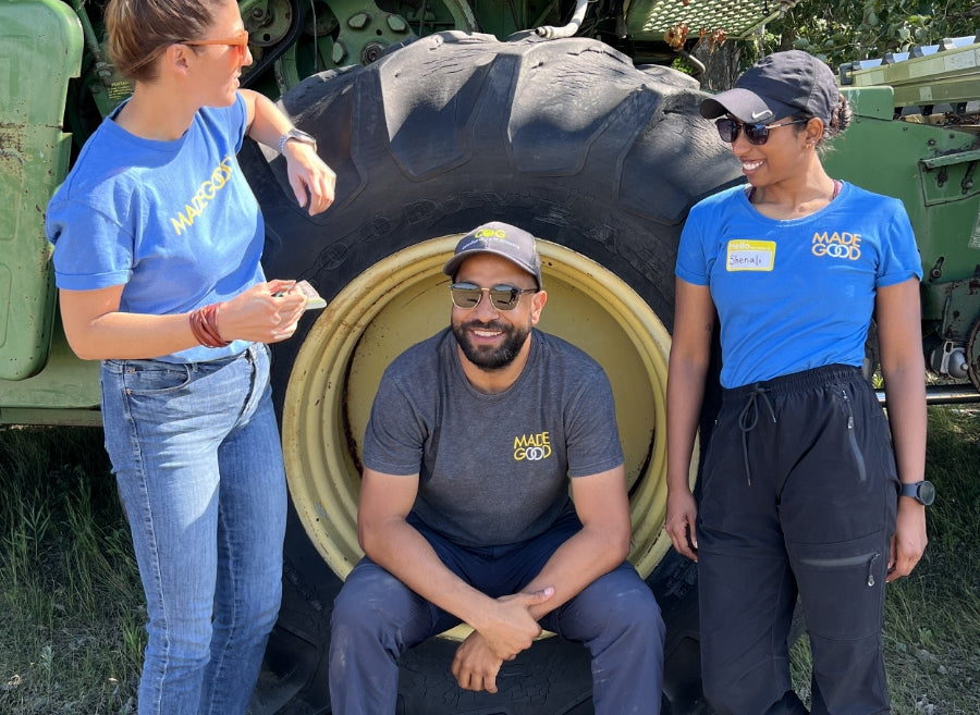 Three MadeGood staff wearing company shirts share a moment in front of a tractor wheel.