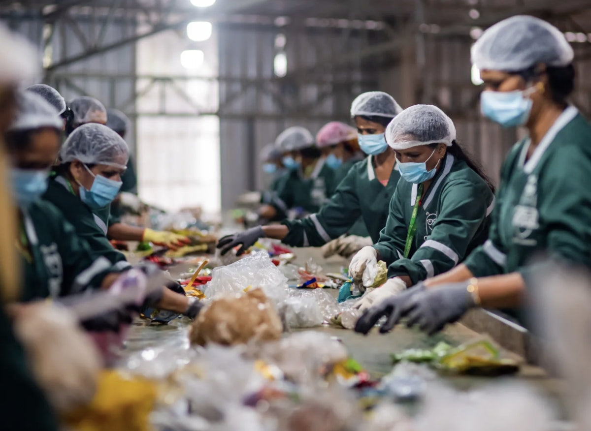 A line of workers wearing PPE work on a conveyor belt to sort garbage