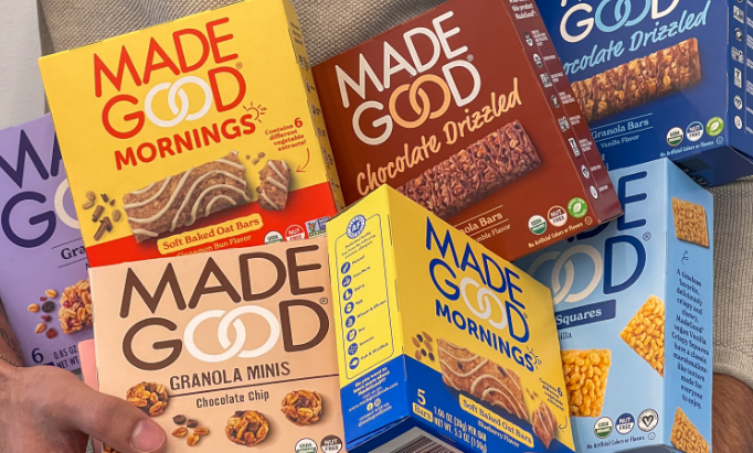 A variety of colorful Made Good snack boxes, including oat bars and granola minis, are held together, showcasing different flavors and packaging designs.